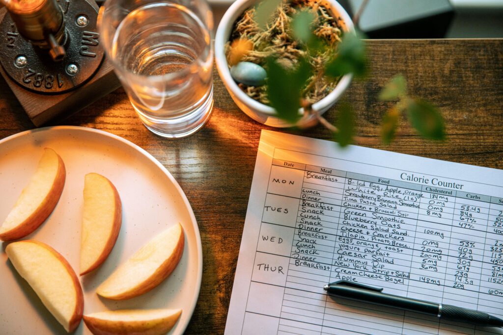 Top view of apple slices, water, and a calorie counter sheet on a wooden table promoting a healthy lifestyle.